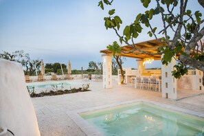 A pool area with a pergola, lounge chairs, and a covered seating area.