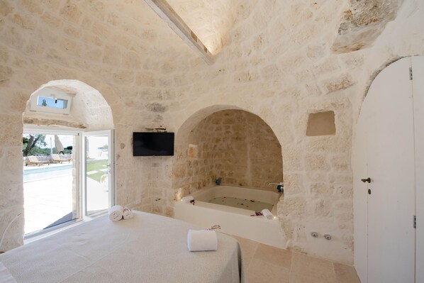 A stone-walled bathroom with a bathtub, a shower, and a large window.