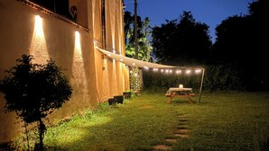 A building with a balcony, a string of lights, and a grassy area with a wooden swing set.