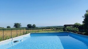 A rectangular swimming pool with clear blue water, surrounded by a fence and vegetation.