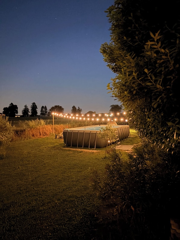 A swimming pool surrounded by a grassy area with string lights in the background.