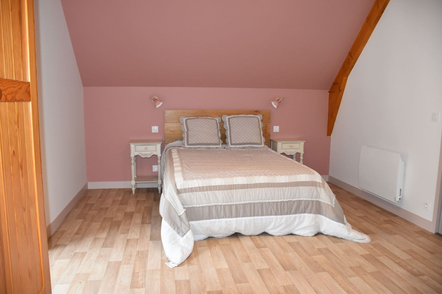 Un dormitorio con suelo de madera, una cama con colcha a rayas, dos mesitas de noche y un calentador de pared.