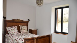 A bedroom with a wooden bed, floral bedding, a nightstand, a small table, and a window with a view. - Gite Le Paradis (Lacave)