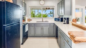 Een moderne keuken met grijze kastjes, een zwarte koelkast en een raam met uitzicht op palmbomen.