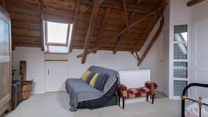 A loft bedroom with a sloped ceiling, a bed, a bench, and a window.