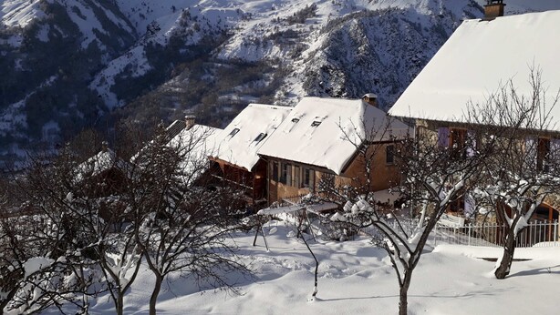 A snow-covered mountain landscape with a building featuring a sloped roof and a chimney.