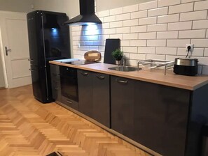 Une cuisine moderne avec un parquet en bois disposé en chevrons, des meubles de couleur sombre, une hotte noire et un évier en acier inoxydable.