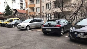 En parkeringsplats med flera parkerade bilar, bland annat en vit bil, en silverfärgad bil och en svart bil.