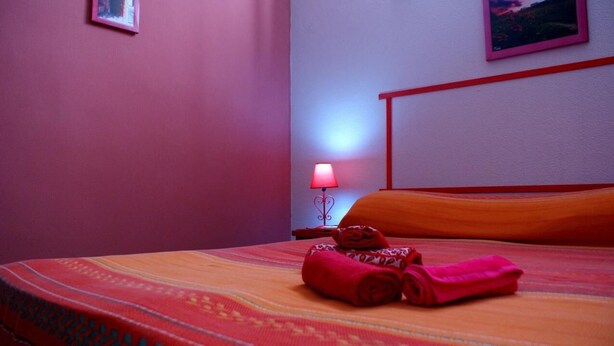 A neatly made bed with a striped bedspread, a red lamp on a bedside table, and a wall-mounted picture. - LG Affittacamere Acireale (Acireale)