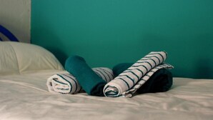 A bed with rolled towels and a pillow against a teal wall. - LG Affittacamere Acireale (Acireale)