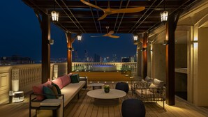 Une terrasse sur le toit, aménagée avec un canapé, des chaises et une table, d’où l’on peut admirer la vue sur la ville illuminée la nuit.