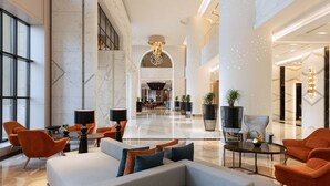 Un hall d’entrée spacieux au design moderne, comprenant un grand espace salon avec des canapés et des fauteuils, une table basse centrale et un lustre.