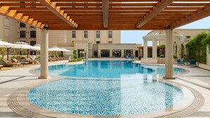 Une piscine surmontée d’une pergola en bois, entourée de chaises longues et de parasols.
