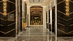 Un hall d’hôtel luxueux, doté d’un sol en marbre, d’un comptoir de réception et d’une grande porte en arc donnant accès aux chambres de l’hôtel.