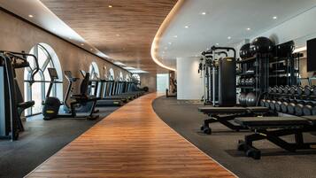 A modern gym with cardio machines, weightlifting equipment, and dumbbells.