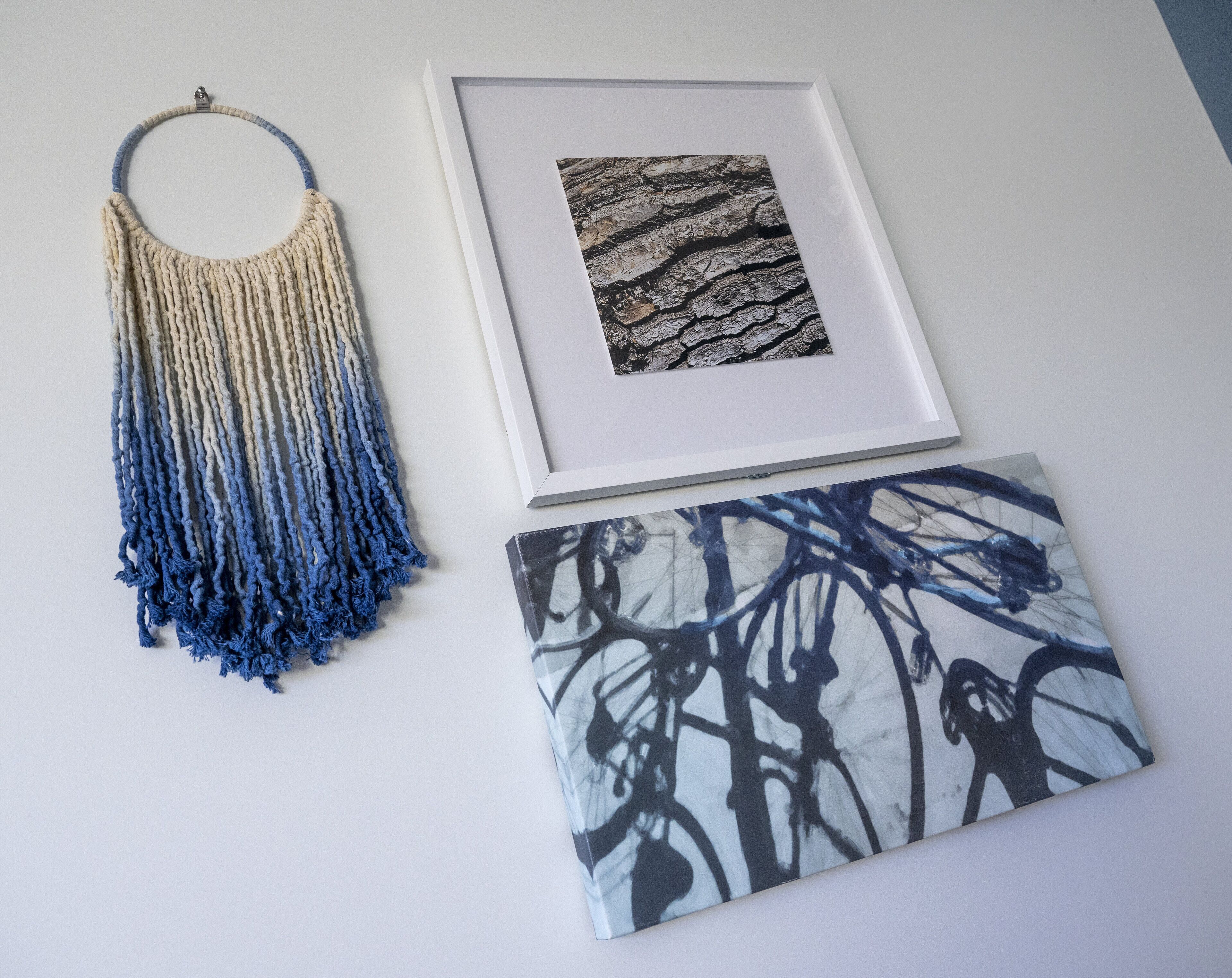 A macrame wall hanging, a framed photograph, and a canvas with abstract art.