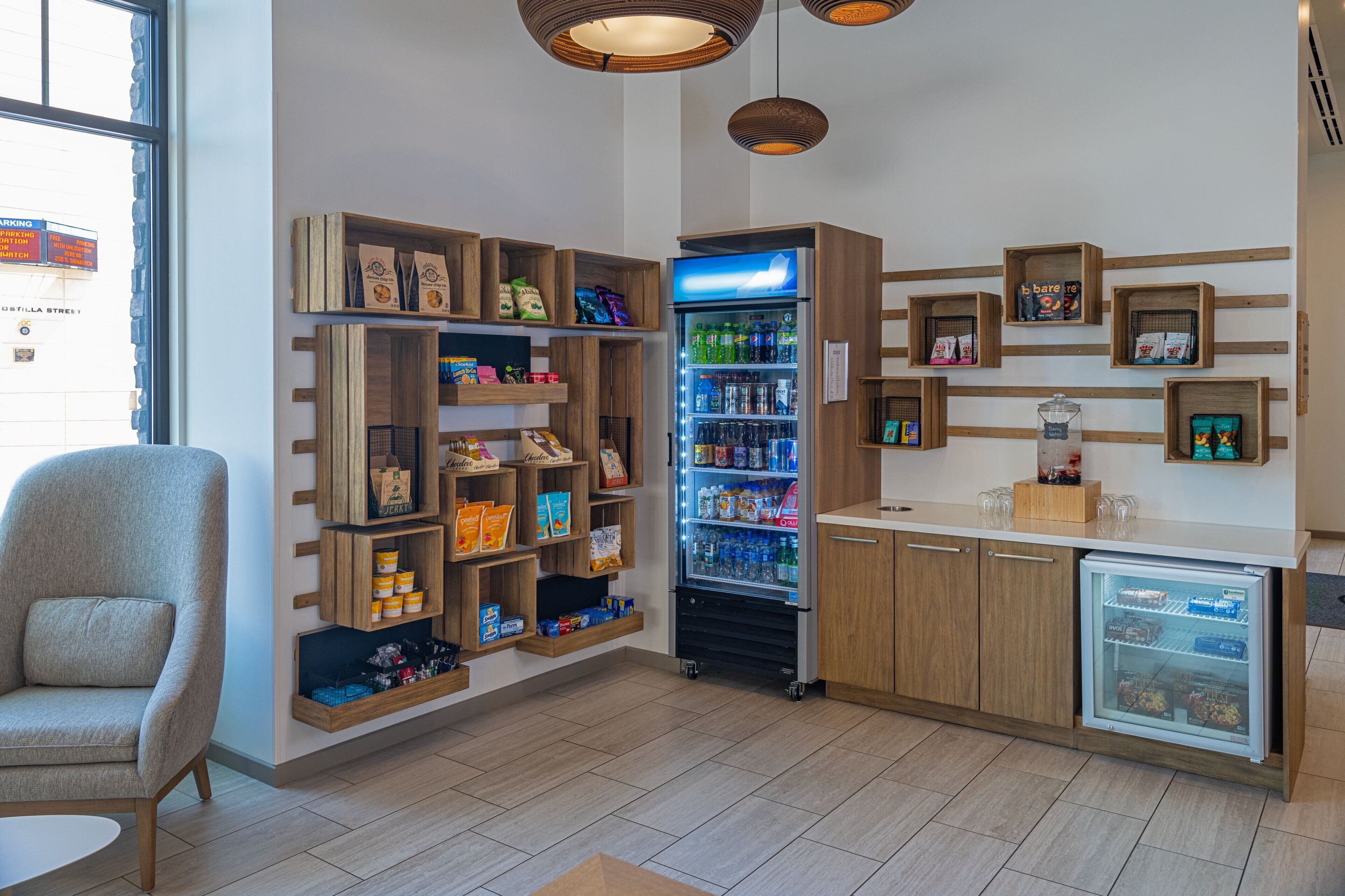 A modern interior with wooden shelves displaying snacks and beverages, a seating area, and a refrigerator.