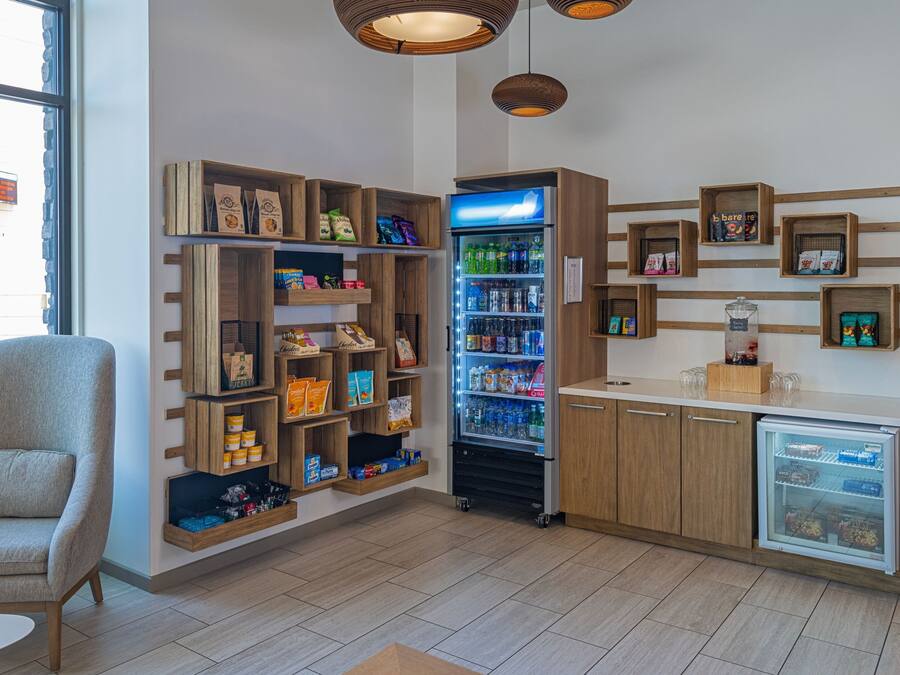 A modern interior with wooden shelves displaying snacks and beverages, a seating area, and a refrigerator.