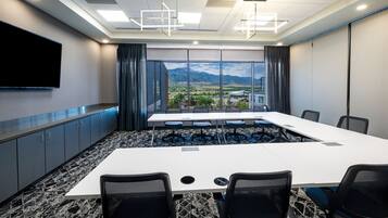 A conference room with a large table, chairs, a flat-screen TV, and a view of a cityscape through large windows.
