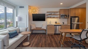 A modern hotel room with a sofa, a small round table, a dining table with chairs, a kitchen area with a microwave and refrigerator, and a large window offering a city view. - Element by Marriott Colorado Springs Downtown (Colorado Springs)