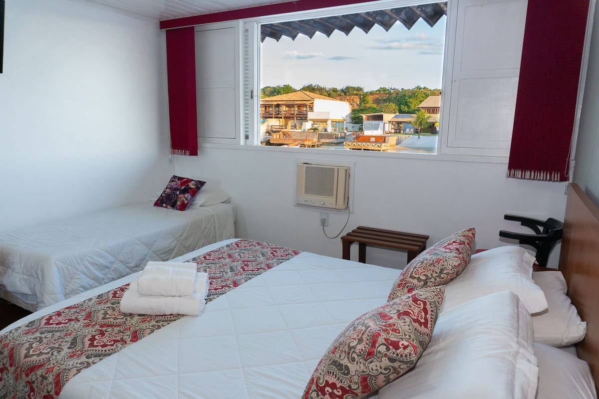 A hotel room with two beds, a window with a view of buildings and a truck, and a small table with a phone.