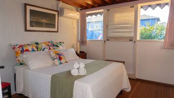 A neatly made bed with a white comforter and pillows, a green throw blanket, and rolled towels on the bed.