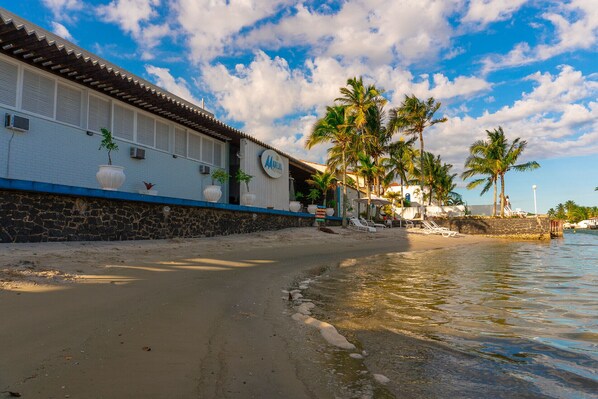 Un edificio costero con tejado de baldosas, pared de piedra y una playa arenosa.