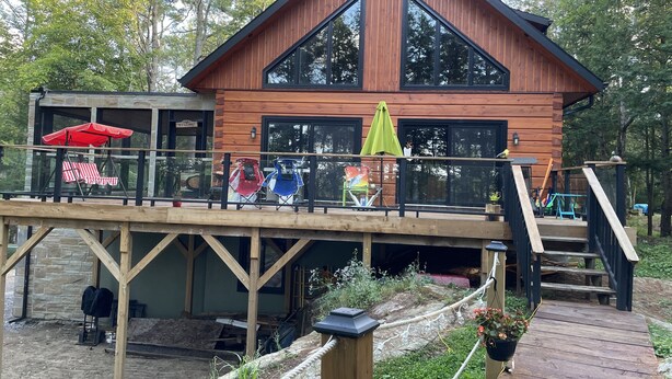 Una cabaña de madera con un porche, ventanas grandes y un letrero que dice 'Welcome'.