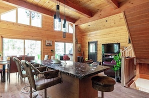A wooden cabin interior with a dining area, a large window, and a television.