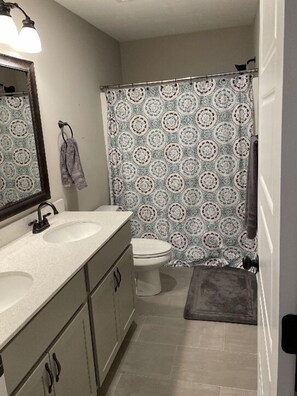 Baño con tocador doble lavabo, inodoro y cortina de ducha con diseño estampado.
