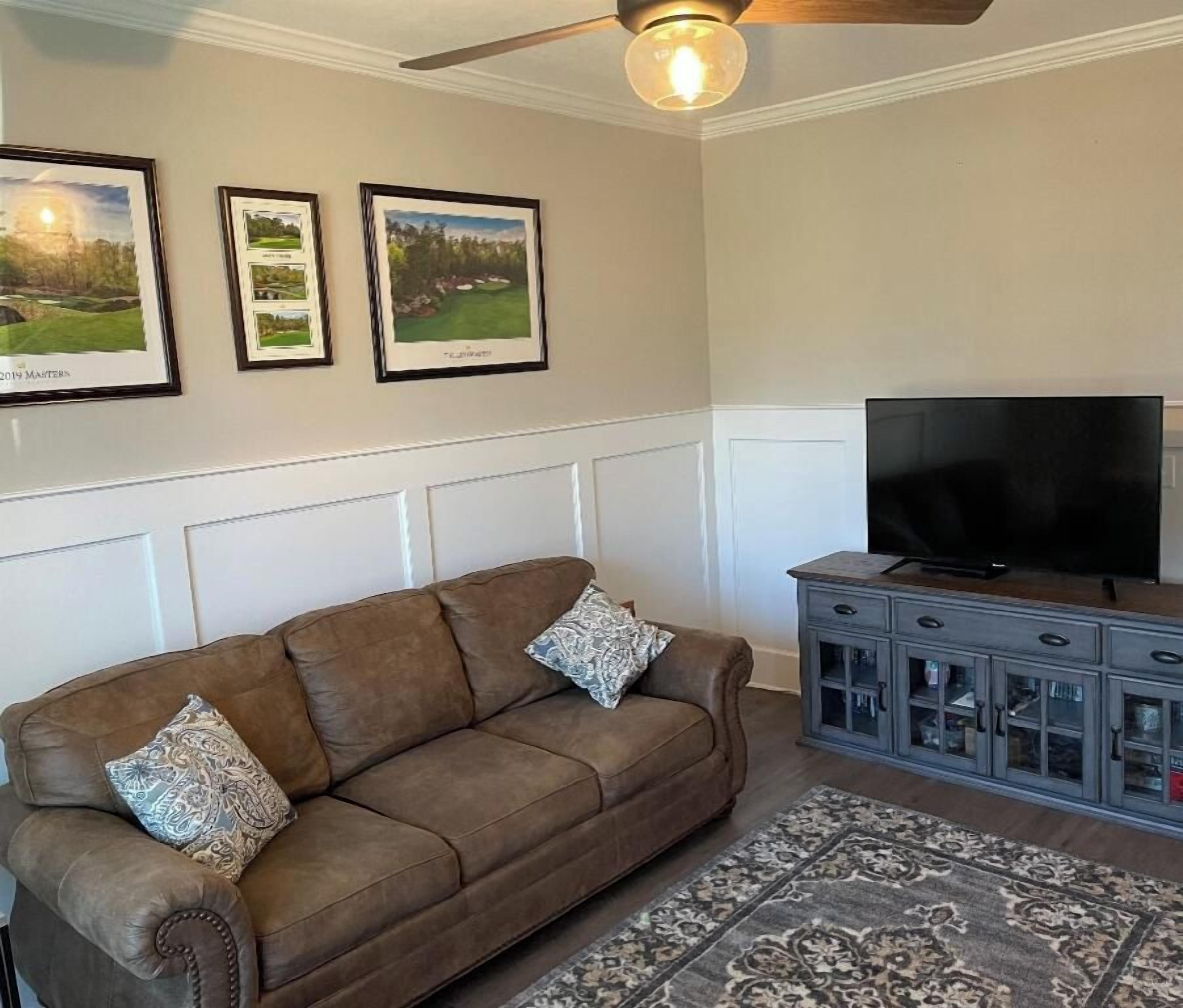 A living room with a brown sofa, patterned cushions, a flat-screen TV, and a gray cabinet with glass doors.