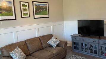 A living room with a brown sofa, patterned cushions, a flat-screen TV, and a gray cabinet with glass doors.