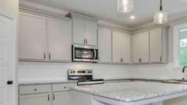 A kitchen with white cabinetry, a central island, a microwave, and a dishwasher. - 2027 Masters Rental Augusta GA (Harlem)