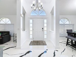 A spacious entryway with a white door, a chandelier, and a bench.