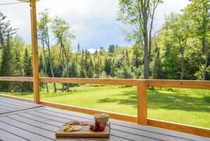 A wooden deck with a table set for a meal, overlooking a forested area. - Cozy 3 Bedroom Cabin in the Adirondack Foothills (Boonville)