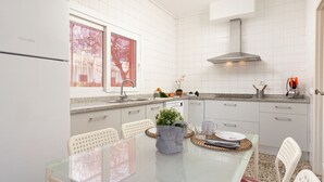 Une cuisine moderne avec des meubles blancs, une hotte en acier inoxydable et un coin repas comprenant une table en verre et des chaises blanches.