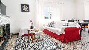 Une pièce avec un canapé blanc, une petite table sur laquelle est posé un vase, une cheminée et une vue sur l’extérieur.
