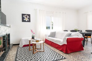 A room with a white sofa, a small table with a vase, a fireplace, and a view of the outdoors.