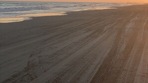Una spiaggia con una lunga distesa di sabbia e un molo in lontananza.