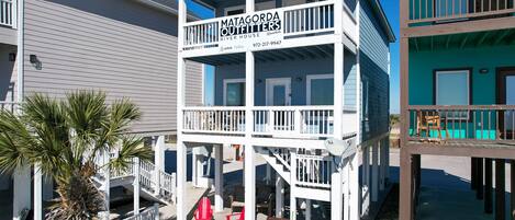 Un edificio de varios pisos con un letrero que indica Matagorda Outfitters River House Rentals, con balcones y asientos al aire libre.