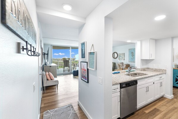 A modern kitchen with white cabinetry, a dishwasher, and a granite countertop. - Sandcastle Condominiums Unit 113 (Port Aransas)