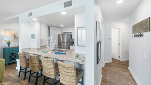 A modern kitchen with a central island, bar stools, and a dining area. - Sandcastle Condominiums Unit 113 (Port Aransas)