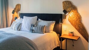 En pænt redt seng med mørkt sengegavl, flere puder og et natbord med lampe og en kasse med bind.