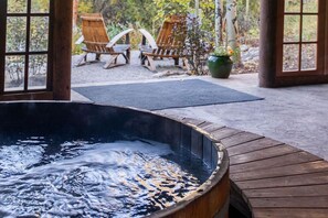 A hot tub with a wooden deck, two wooden chairs, and a potted plant in a covered outdoor area. - Rocky Mountain Retreat with Hot Tub + Barrel Sauna (Allenspark)