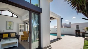 A modern living room with a glass coffee table, a sofa with yellow cushions, a yellow armchair, and a sliding glass door leading to a pool area. - VILLA ORCADES CLOSE TO TOWN CENTER POOL & A/C (Playa Blanca)