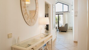 A modern bathroom with a round mirror, a glass console table, and a view into a living area with a sofa and a window. - VILLA ORCADES CLOSE TO TOWN CENTER POOL & A/C (Playa Blanca)