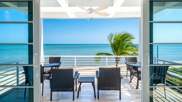 A balcony with a view of the ocean, wicker furniture, and a ceiling fan.
