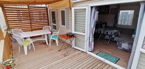 A covered outdoor area with a table and chairs, a wooden deck, and a view into the interior of a house.