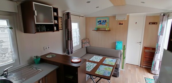 A compact kitchen with a sink, a small table with a decorative mat, a cabinet with dishes, and a door with a sign.