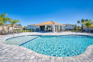 Une piscine avec une terrasse carrelée, un espace salon couvert et des palmiers.